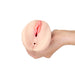 Hand holding a compact, flesh-toned dual-opening stroker with detailed texture and soft pink accents.