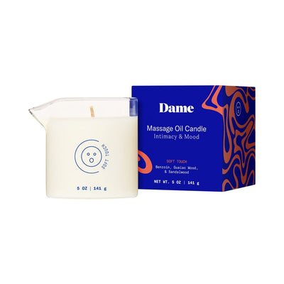 Dame Massage Oil Candle in clear glass with easy-pour spout next to blue and orange patterned box packaging.