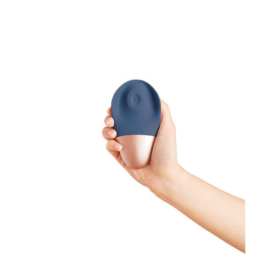 Hand holding the Deia The Arouser silicone device in blue with rose gold base, designed for external stimulation.