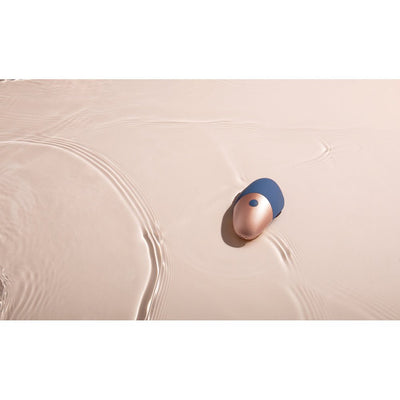 Compact blue and rose gold silicone arouser floating on water surface with gentle ripples.