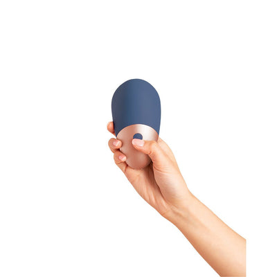 Hand holding the Deia The Arouser silicone device in blue with rose gold accent and single button control.