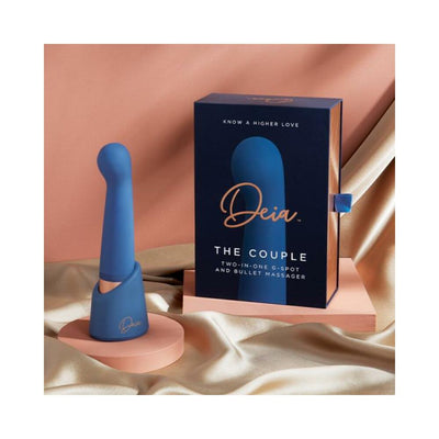 Blue silicone Deia The Couple two-in-one G-spot and bullet massager with packaging on soft fabric background.