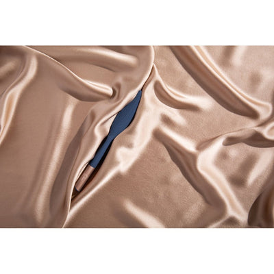 Blue feather-shaped silicone vibrator resting on smooth beige satin fabric.