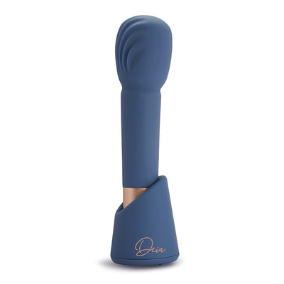 Blue silicone Deia The Wand with textured head standing in matching charging stand on white background.