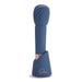 Blue silicone Deia The Wand with textured head standing in matching charging stand on white background.