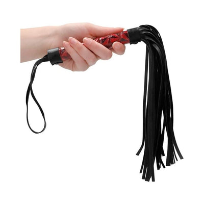 Hand holding a burgundy diamond-patterned faux-leather whip with black leather strands and wrist loop.