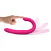 Hand demonstrating the flexible pink Dorcel Orgasmic Double Do vibrator with dual curved ends on white background.