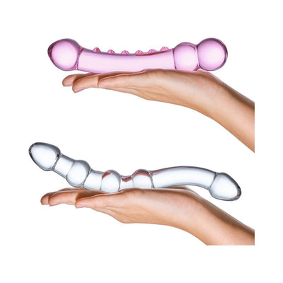 Two hands holding a set of two textured glass dildos, one pink and one clear, showcasing their smooth and curved designs.