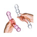 Hands holding two double-ended glass dildos, one clear and one pink, with smooth and textured designs.