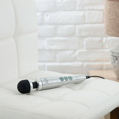 Compact silver Doxy Die Cast 3 wand vibrator with black silicone head resting on a white cushioned chair.