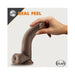Hand holding a chocolate-colored 7-inch realistic dildo with balls and suction base, labeled real feel by Blush.