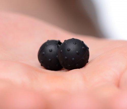 Close-up of two black nubbed silicone-coated magnetic spheres resting on a person's palm.