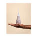 Hand holding a soft silicone anal douche with a white removable tip against a beige background.