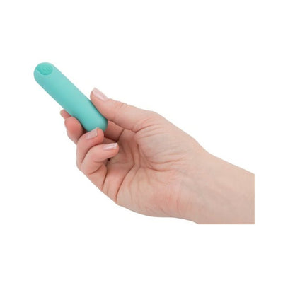 Hand holding a compact teal rechargeable vibrating bullet with a smooth matte finish and power button on top.