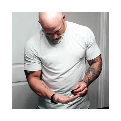 Man with tattoos and a white shirt applying beard oil from a dropper onto his palm.