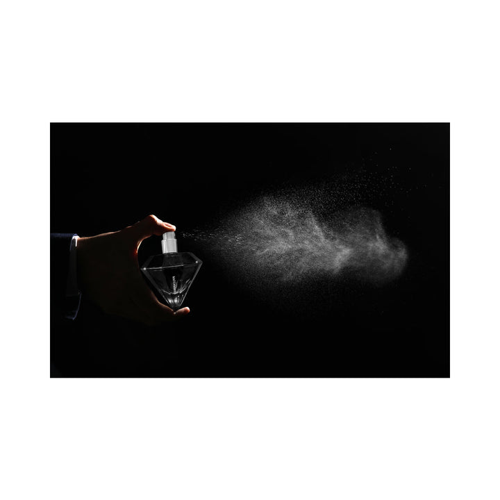Hand spraying Eye of Love Matchmaker Pheromone Perfume Black Diamond in a diamond-shaped bottle with mist against black background.