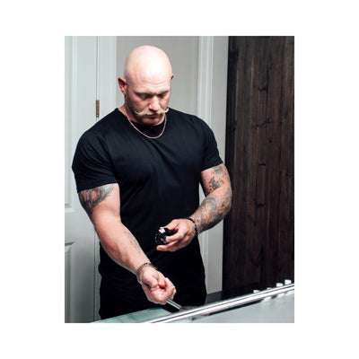 Man with tattoos applying Eye of Love Matchmaker Pheromone Perfume Black Diamond on wrist in front of mirror