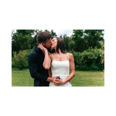 Couple embracing and kissing outdoors with woman holding Eye of Love Matchmaker Pheromone Perfume bottle in hand.