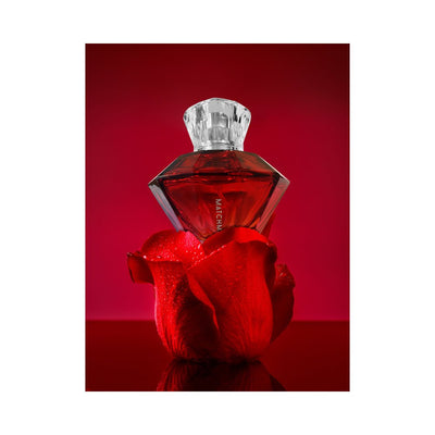Red diamond-shaped perfume bottle with clear cap resting on a red rose petal against a red background.