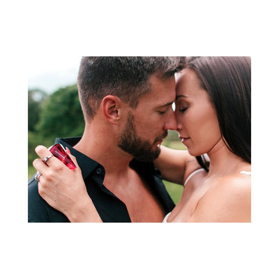 Couple sharing an intimate moment outdoors with woman holding Eye of Love Matchmaker Pheromone Perfume Red Diamond bottle.