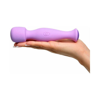 Hand holding a compact lavender silicone body massager with a rounded head and power button on the handle.