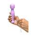 Hand holding a compact purple silicone body massager while plugging in a USB charging cable.