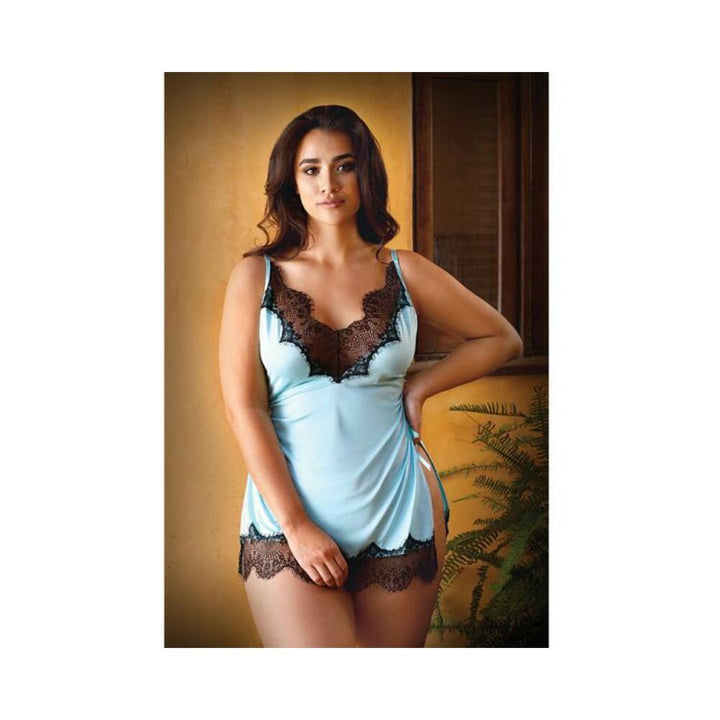 Woman wearing powder blue chemise with black lace trim and adjustable straps, posing indoors by a window and plants.