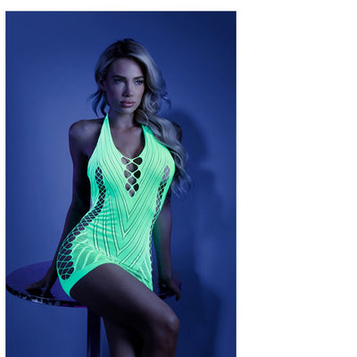 Model wearing neon green glow net halter dress with open back, sitting on a round table against a dark blue background.