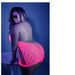 Plus size model wearing neon pink glow net halter dress with open back and geometric patterns, posing by a small round table.