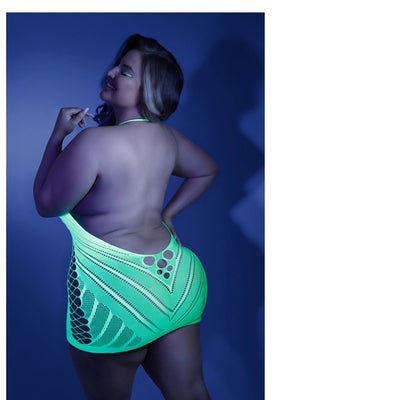 Plus size model wearing a neon green glow net halter dress with an open back under blue lighting.