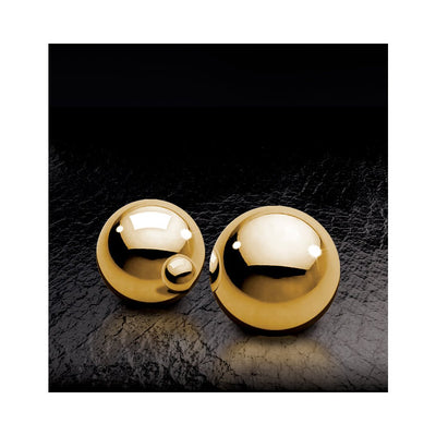 Two polished gold metal Ben Wa balls on a textured black surface with reflective highlights.
