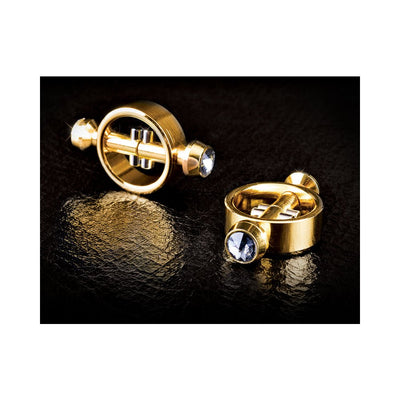 Pair of gold magnetic nipple clamps with clear jeweled accents on black textured surface