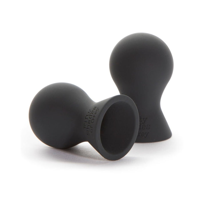 Pair of black silicone nipple teasers with rounded tops and flared bases, embossed with Fifty Shades of Grey logo.