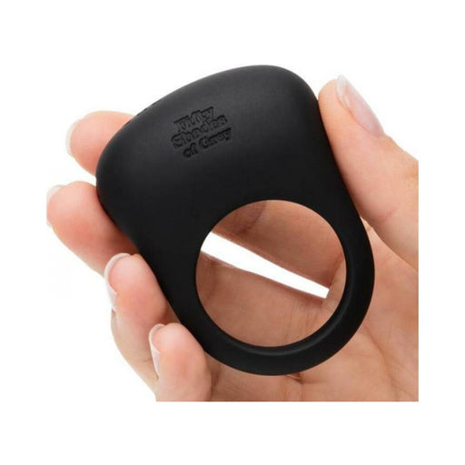 Hand holding a sleek black silicone vibrating love ring from Fifty Shades of Grey with a textured pad and circular design.
