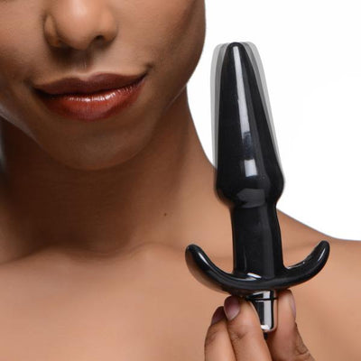 Close-up of a person holding a sleek black vibrating anal plug with a tapered tip and curved base.