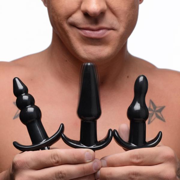 Man holding three black anal plugs in different shapes from the Frisky Thrill Anal Plug Set against a white background.