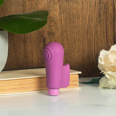 Purple Blush Gaia Eco Delight vibrator standing on a white surface with a book, green leaf, and white flower background.