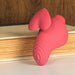 Coral pink eco-friendly vibrator with heart-shaped fin and ribbed tip resting on a closed book against a wood background.