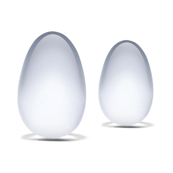 Two smooth, translucent glass yoni eggs in teardrop shapes, displayed on a white background.