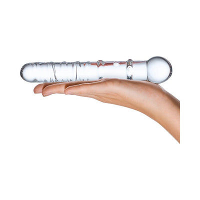 Hand holding a clear glass dildo with textured spirals and rounded tip on a white background.