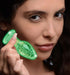 Close-up of a woman holding a small glow-in-the-dark glass anal plug with a green luminous swirl.