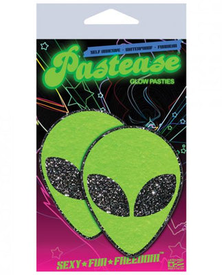 Package of green glitter alien-shaped pasties with black glitter eyes by Pastease on colorful starry background.