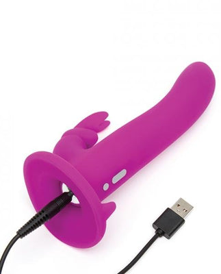 Purple silicone vibrating strap-on shaft with clitoral stimulator and USB charging cable connected.