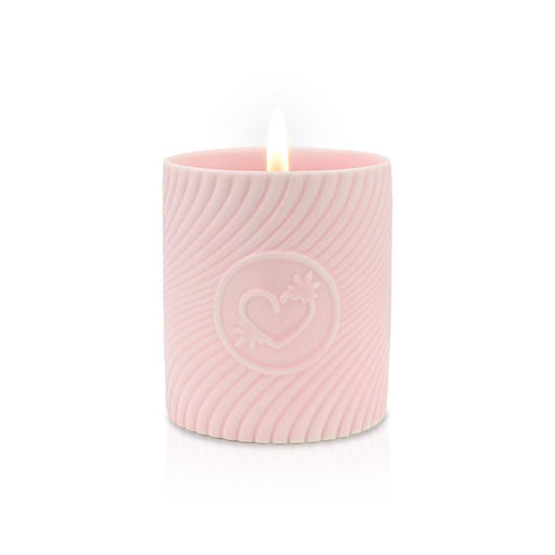 Lit pink massage candle in a textured container with embossed heart design, creating a warm, romantic ambiance.