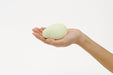 Hand holding a smooth, rounded pale green Iroha Midori massager with a soft, ergonomic shape.
