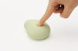 Hand pressing the smooth, rounded green Iroha Midori massager with soft silicone surface on white background.