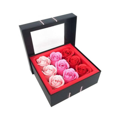 Elegant black gift box with nine rose-shaped soap petals in shades of pink and red arranged in a red interior tray.