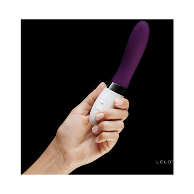 Hand holding a sleek purple and white LELO Liv 2 personal massager with ergonomic control buttons against a black background.