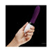 Hand holding a sleek purple and white LELO Liv 2 personal massager with ergonomic control buttons against a black background.