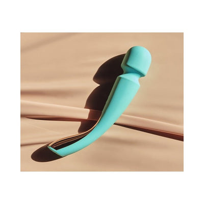 Lelo Smart Wand 2 Large in turquoise with ergonomic curved design resting on a beige surface with soft shadows.